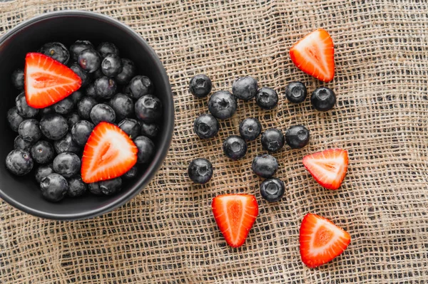 Vue de dessus des bleuets entiers et des fraises coupées sur le sac — Photo de stock