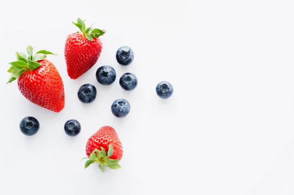 Blaubeeren und Erdbeeren von oben mit grünen Blättern auf weißer Oberfläche — Stockfoto