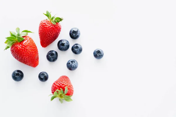 Top view of blueberries and strawberries with green leaves on white surface — Stock Photo