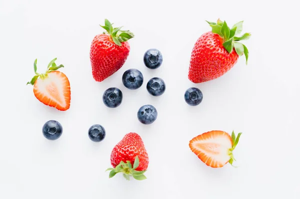 Vue du dessus des bleuets près des fraises coupées sur fond blanc — Photo de stock