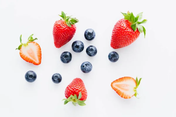 Vista superior de arándanos cerca de fresas cortadas sobre fondo blanco - foto de stock