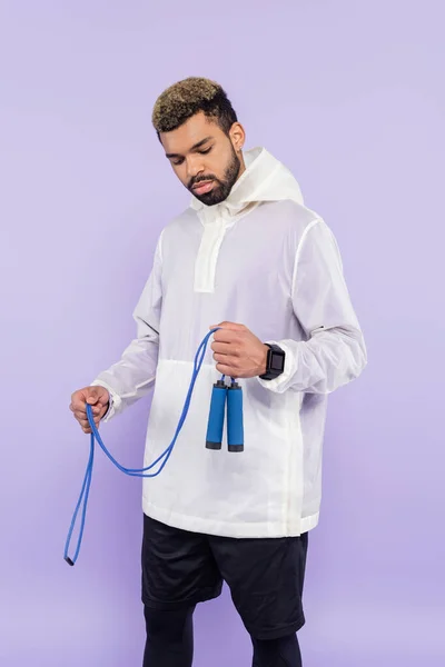 Молодий афроамериканський чоловік у модному спортивному одязі, що тримає пропускаючу мотузку ізольовано на фіолетовому — стокове фото