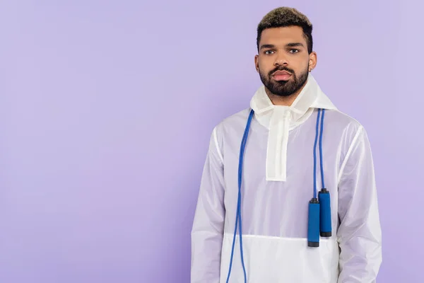 Young african american man in trendy sportswear with skipping rope isolated on purple — Stock Photo