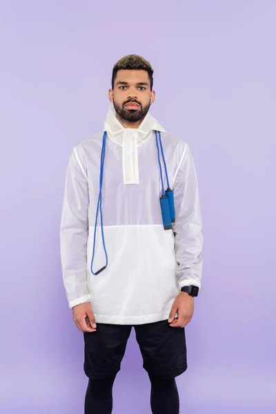 Young african american man in stylish sportswear standing with skipping rope isolated on purple — Stock Photo