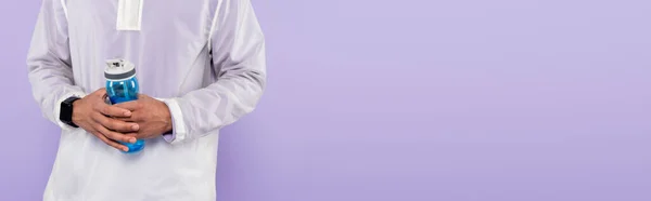 Cropped view of african american man in trendy sportswear holding sports bottle isolated on purple, banner — Stock Photo