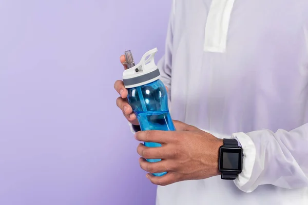 Partial view of african american man in trendy sportswear holding sports bottle isolated on purple — Stock Photo