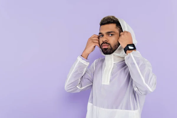 African american sportsman in stylish sportswear wearing hood looking at camera isolated on purple — Stock Photo