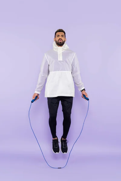 Longueur totale de sportif afro-américain en sportswear sautant avec corde à sauter sur violet — Photo de stock