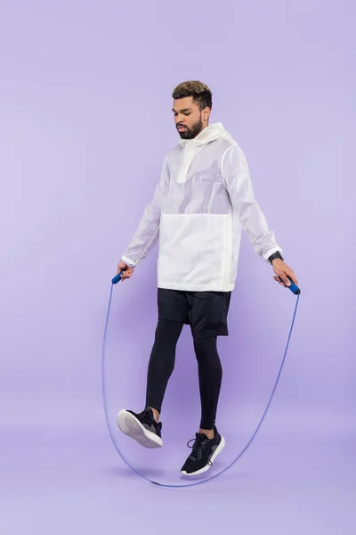 Full length of african american sportsman in sportswear exercising with skipping rope on purple — Stock Photo