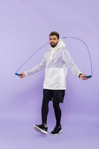 Full length of young african american sportsman in sportswear exercising with skipping rope on purple — Stock Photo