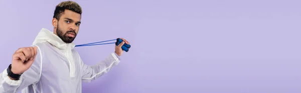 Barbudo afroamericano deportista sosteniendo saltar la cuerda aislado en púrpura, bandera — Stock Photo