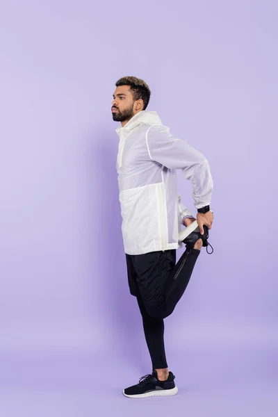 Full length of young african american man in sportswear warming up on purple — Stock Photo