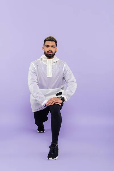 Full length of bearded african american sportsman in sportswear doing lunges on purple — Stock Photo