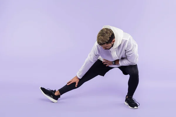 Full length of african american sportsman in sportswear doing lunges on purple — Stock Photo