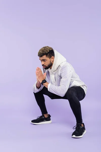 Повна довжина бородатого афроамериканського спортсмена в спортивному одязі, що працює з молитовними руками на фіолетовому — стокове фото