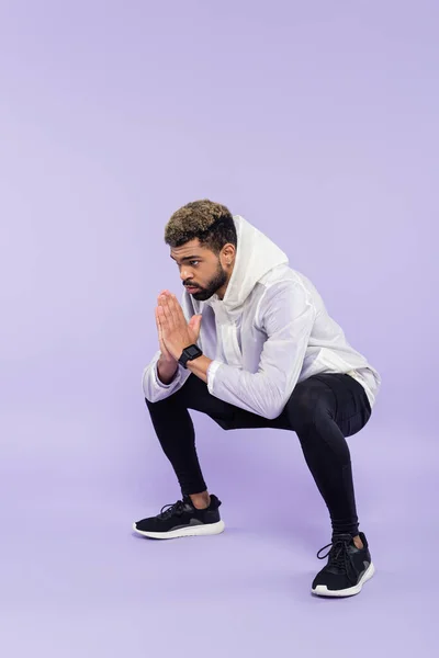 Comprimento total de desportista americano africano barbudo em sportswear trabalhando com as mãos orando em roxo — Fotografia de Stock