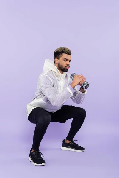 Toute la longueur de barbu sportif afro-américain faisant squat avec haltère sur violet — Photo de stock