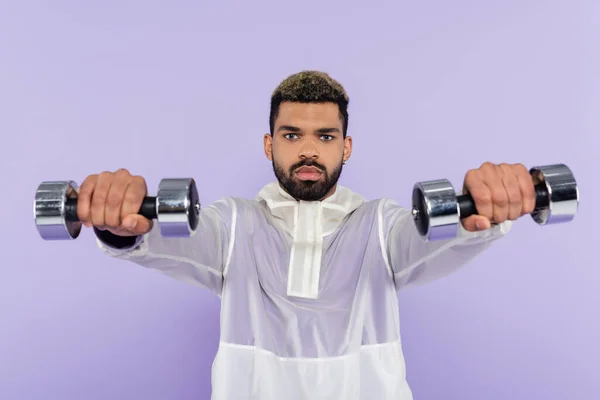Bearded african american man exercising with dumbbells isolated on purple — Stock Photo