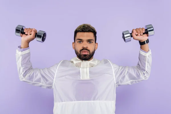 Jovem afro-americano exercitando com halteres isolados em roxo — Fotografia de Stock