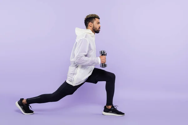 Full length of bearded african american man doing lunges with dumbbells on purple — Stock Photo
