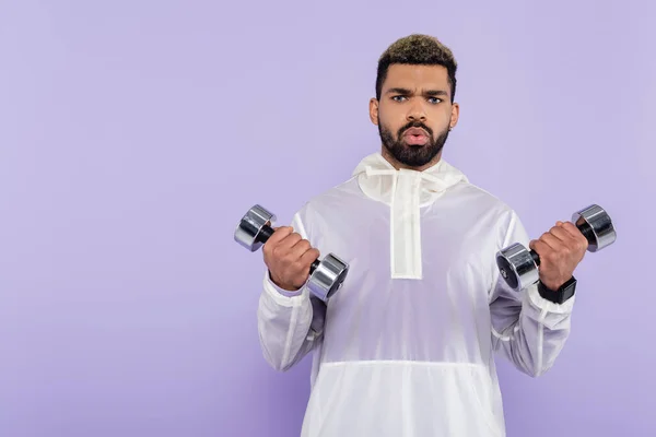 Bearded african american sportsman exercising with heavy dumbbells isolated on purple — Stock Photo