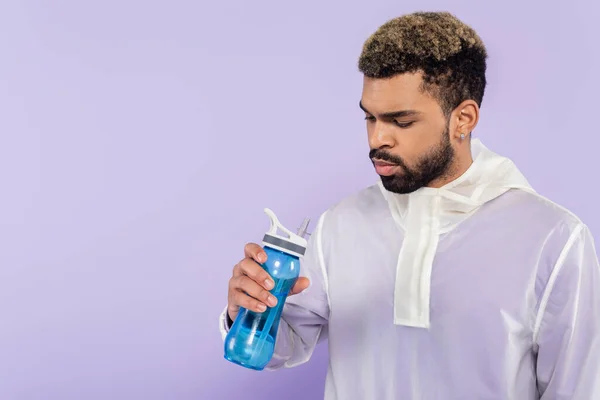 Bearded african american sportsman holding sports bottle with water isolated on purple — Stock Photo