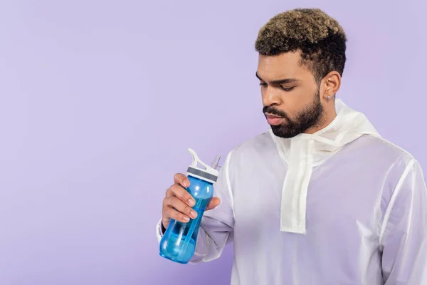 Sportif afro-américain barbu tenant bouteille de sport avec de l'eau isolée sur violet — Photo de stock