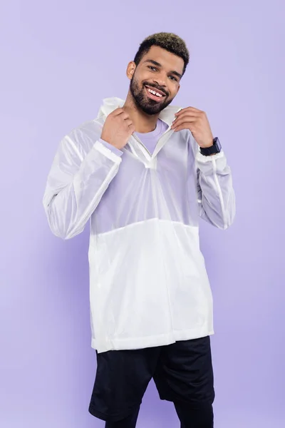 Happy african american sportsman with smart watch adjusting collar isolated on purple — Stock Photo