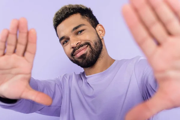 Радісний афроамериканський чоловік в светрі жестикулює і дивиться на камеру ізольовано на фіолетовому — стокове фото