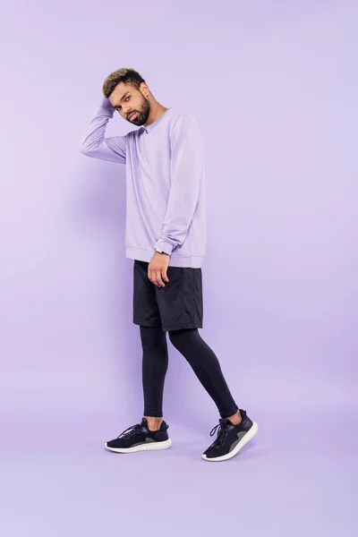 Pleine longueur de barbu homme afro-américain en pull et short debout sur violet — Photo de stock