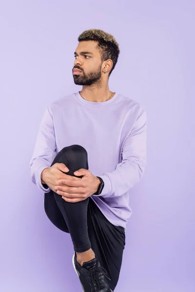 Homme afro-américain barbu en pull regardant loin tout en posant isolé sur violet — Photo de stock