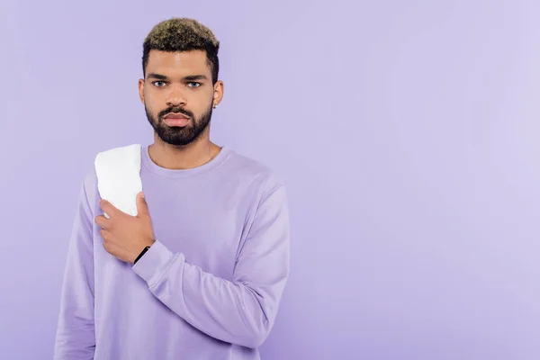 Bearded african american man in sweater holding white towel isolated on purple — Stock Photo