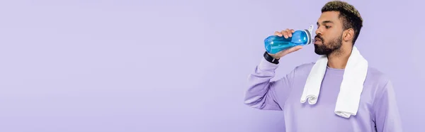 Barbudo hombre afroamericano en suéter de pie con toalla blanca y agua potable aislado en púrpura, pancarta - foto de stock