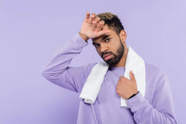 Cansado afro-americano homem em suéter segurando toalha branca e limpando suor com a mão isolada em roxo — Fotografia de Stock