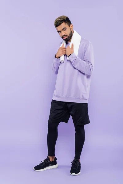 Full length of bearded african american man in sweater holding white towel and looking at camera on purple — Stock Photo