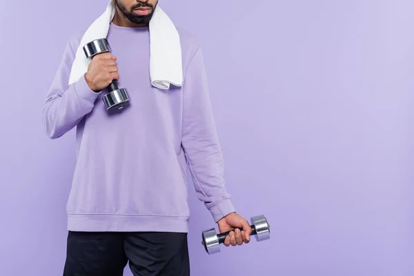 Vue recadrée de barbu homme afro-américain avec serviette d'exercice tout en tenant haltères isolés sur violet — Photo de stock