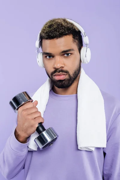 Homem americano africano barbudo em fones de ouvido exercitando com halteres isolados em roxo — Fotografia de Stock