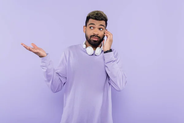 Homem americano africano barbudo com fones de ouvido sem fio falando em smartphone isolado em roxo — Fotografia de Stock