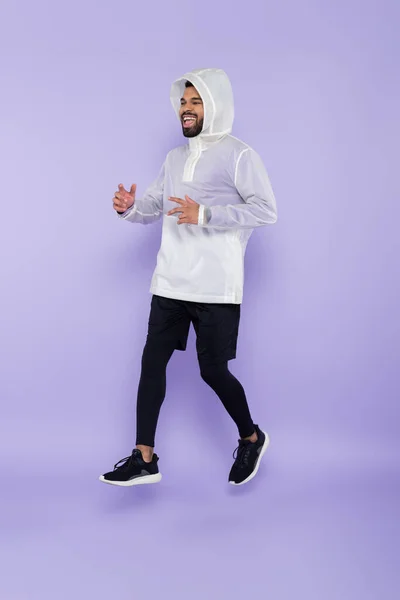 Pleine longueur de joyeux homme afro-américain en vêtements de sport lévitant sur violet — Photo de stock