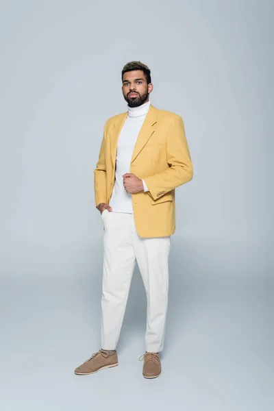 Comprimento total de homem americano africano elegante em blazer amarelo posando em cinza — Fotografia de Stock