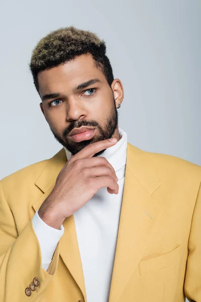 Pensive african american man in stylish yellow blazer posing isolated on grey — Stock Photo