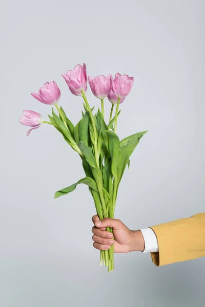 Vista ritagliata dell'uomo afroamericano che tiene bouquet di tulipani rosa isolati sul grigio — Foto stock