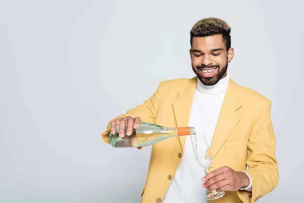 Felice uomo africano americano in abito elegante bottiglia e versando champagne in vetro isolato su grigio — Foto stock