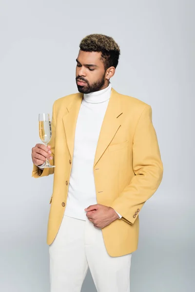 Barbudo hombre afroamericano en traje elegante sosteniendo copa de champán aislado en gris - foto de stock