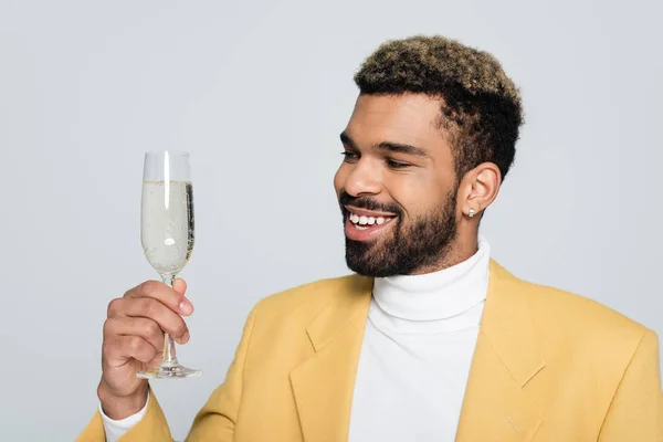 Fröhliche afrikanisch-amerikanische Mann in stilvollem Outfit hält Glas Champagner isoliert auf grau — Stockfoto