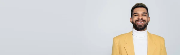 Retrato de hombre afroamericano feliz con ojos azules en traje elegante aislado en gris, bandera - foto de stock