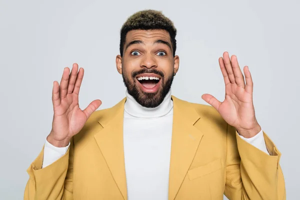 Hombre afroamericano excitado en chaqueta amarilla y cuello de polo aislado en gris - foto de stock