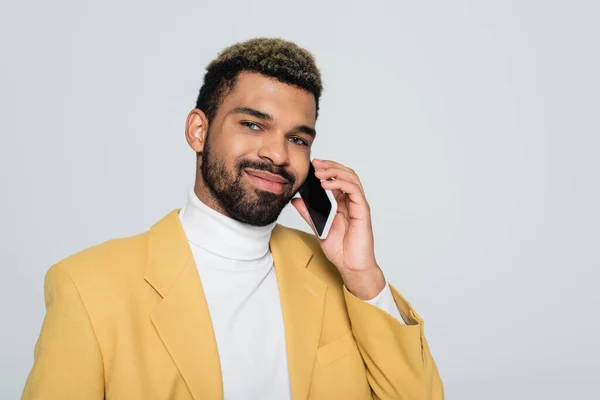 Fröhlicher afrikanisch-amerikanischer Mann im gelben Blazer, der auf seinem Smartphone isoliert auf grau spricht — Stockfoto