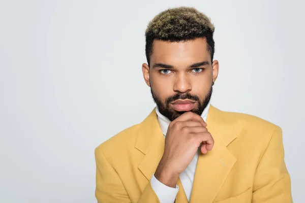 Joven afroamericano hombre con ojos azules en elegante chaqueta amarilla y cuello polo mirando cámara aislada en gris - foto de stock