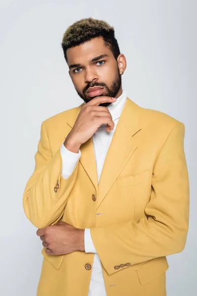 Молодий афроамериканський чоловік з блакитними очима в стильному жовтому блістері дивиться на камеру ізольовано на сірому — стокове фото